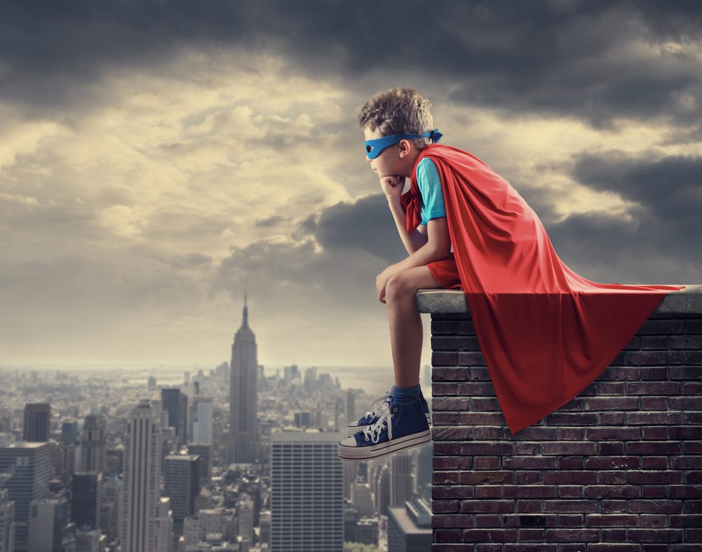 young boy dressed as superman sitting above city view